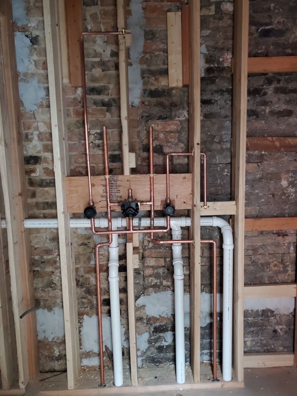 Copper water supply lines and shut-off valves installed inside an exposed brick wall