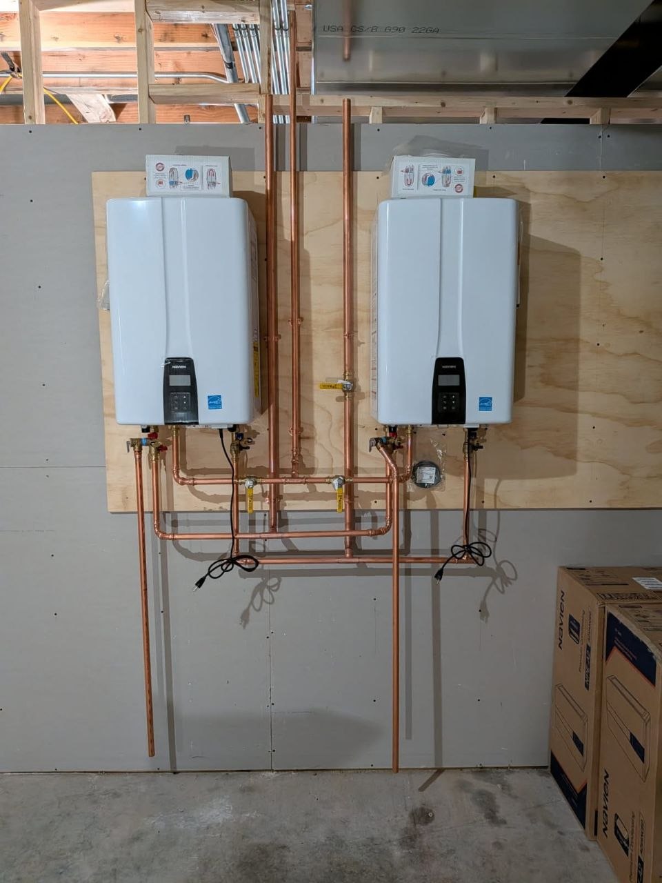 Two tankless water heaters installed with clean copper piping in a residential utility room